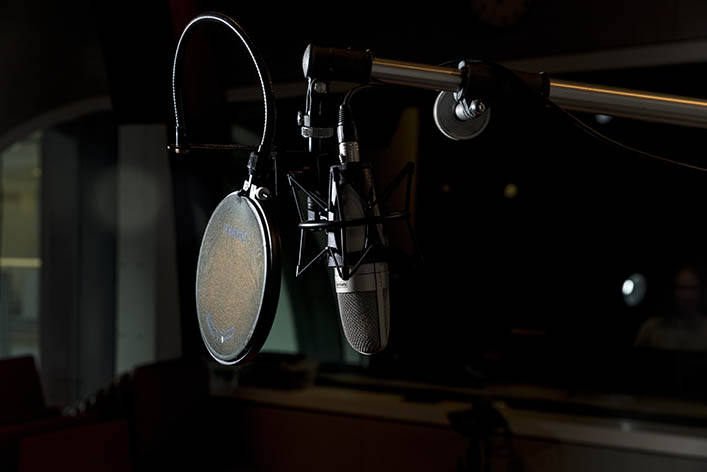 A side-lit photo of a microphone in a recording studio.