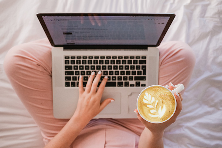 A woman holding a cappuccino while using a laptop. | NYTLicensing