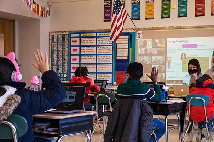 Students in a classroom raise their hands during a lesson.