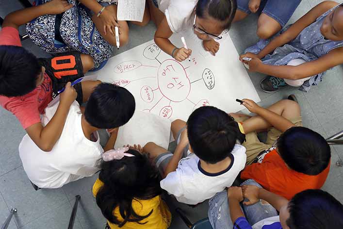 Young students work on a group project. Newspaper articles can be used to teach English in the classroom and beyond.